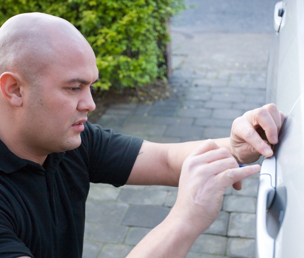 An English-speaking car locksmith holding a transponder chip key beside a vehicle in France